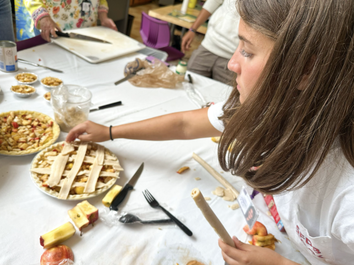 Senior Kate Hyman puts a lattice-crossed crust atop the blend of fruits. “The actual dough was frozen stuck, so we had to use a hair dryer just so we would be able to unroll it. It was still so fun,” said Hyman. 